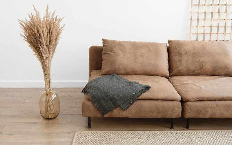 living room with a throw on a couch beside a large floor vase with a plant in it